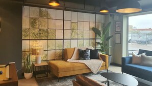 Un salon confortable avec un canapé, une table basse et une lampe. Une grande fenêtre offre une vue sur la rue.