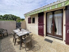 A patio with a table set for two, outdoor seating, and a building with a green awning and a door with a glass panel. - Comfortable house in Argelès - 4 guests (Argelès-sur-Mer)