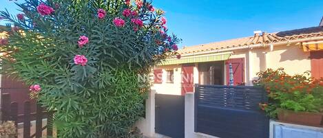 A residential property with a gravel driveway, a metal gate, and a house with a tiled roof.