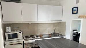 Una cocina compacta con armarios blancos, microondas, estufa, pileta y horno pequeño.