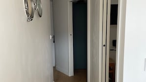 Un pasillo estrecho con suelo de madera, paredes blancas y una puerta que da a una habitación con pared azul oscuro.