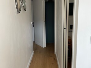 Ein schmaler Flur mit Holzdielen, weißen Wänden und einer Tür zu einem Raum mit dunkelblauer Wand.