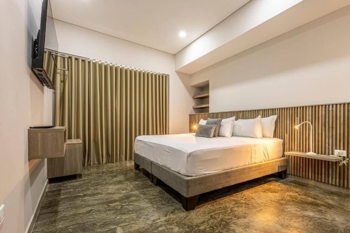 Una habitación de hotel moderna con una cama grande, un televisor de pantalla plana, una mesita de noche y una estantería integrada.