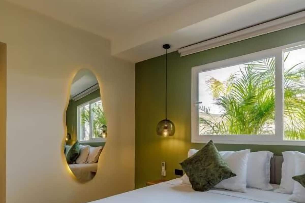 Un dormitorio con una cama, una ventana con vistas a palmeras, un espejo montado en la pared y una lámpara colgante.
