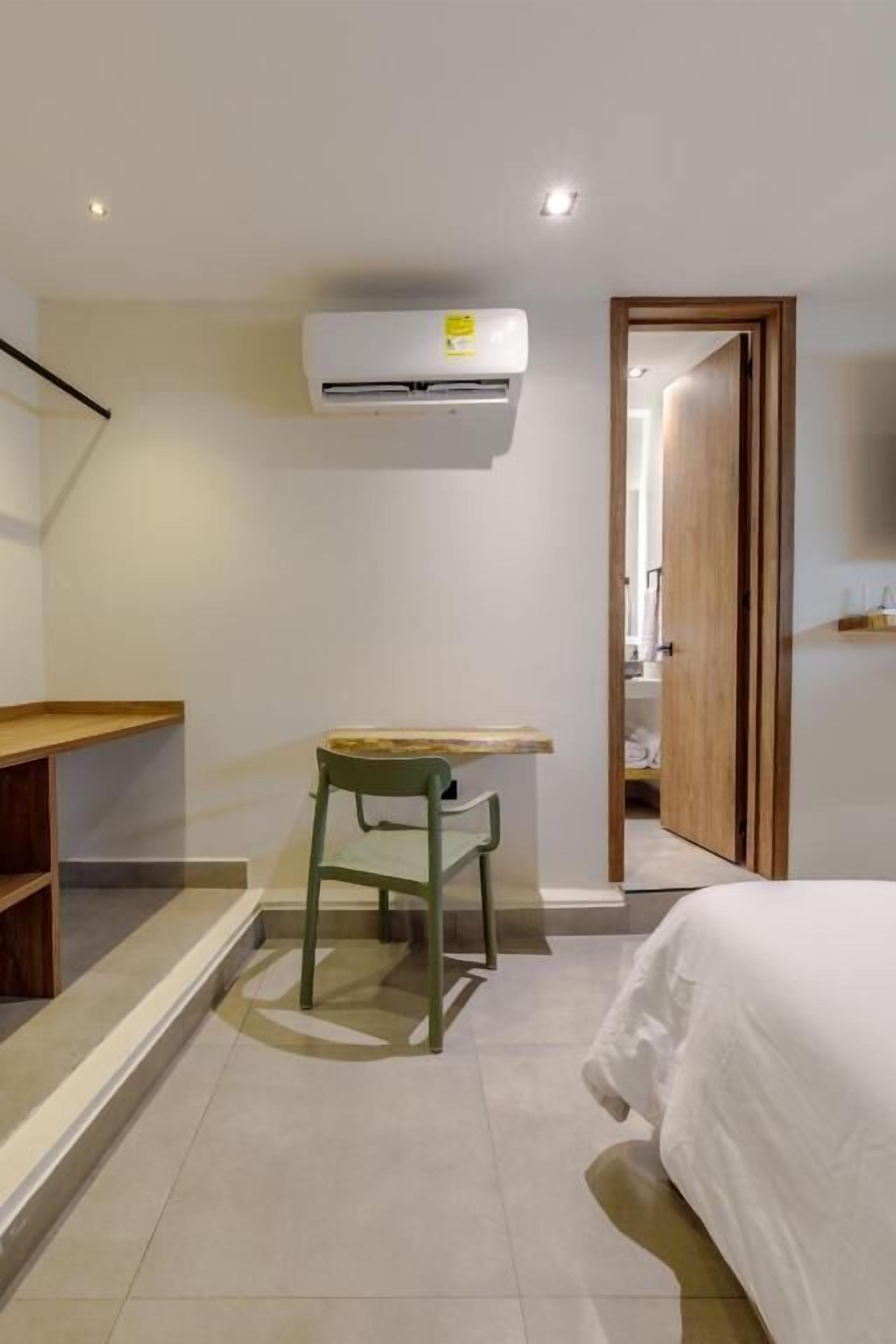 A small, modern room with a bed, a desk, and an air conditioning unit.