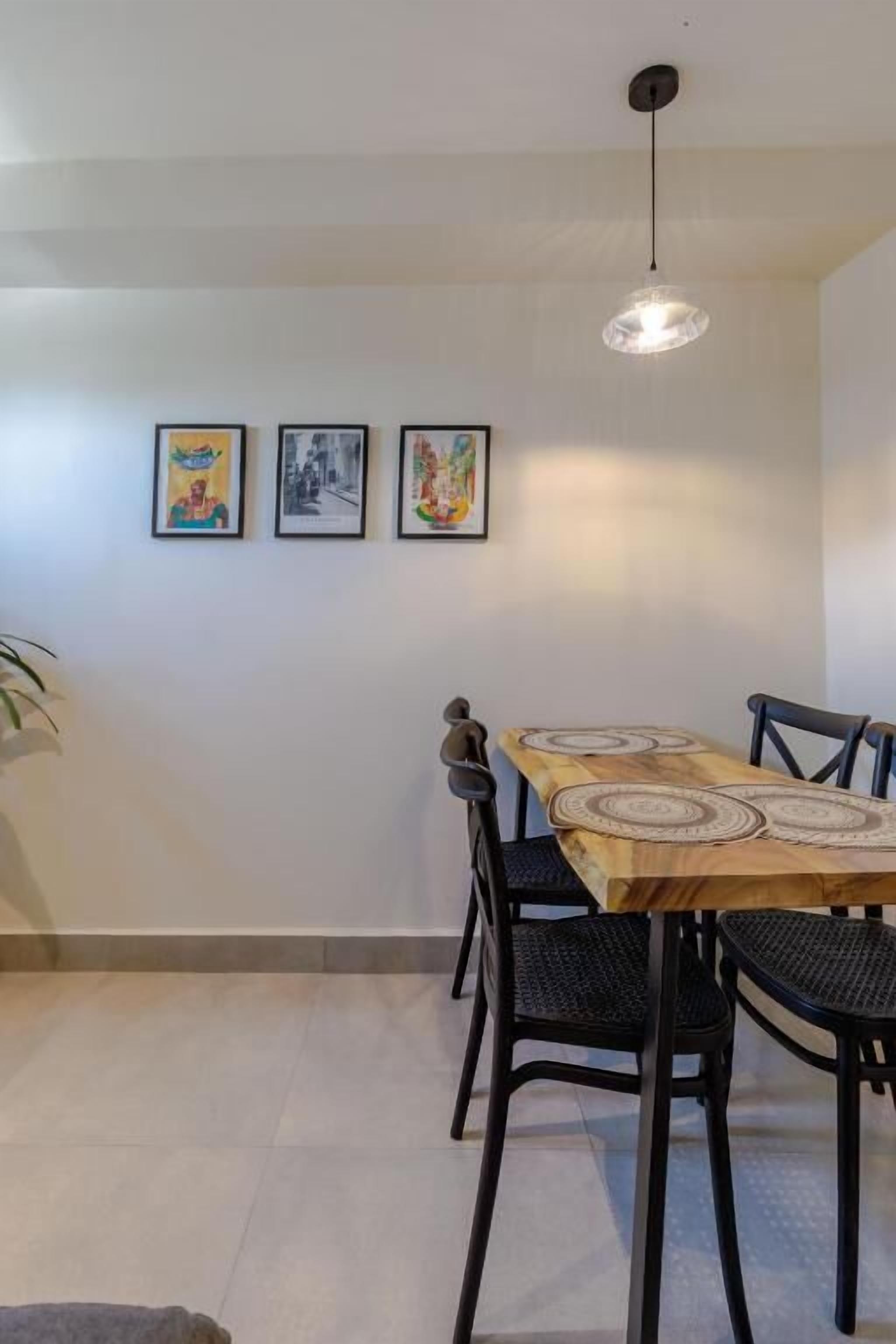 Un espace repas avec une table en bois, des chaises noires et un luminaire suspendu.