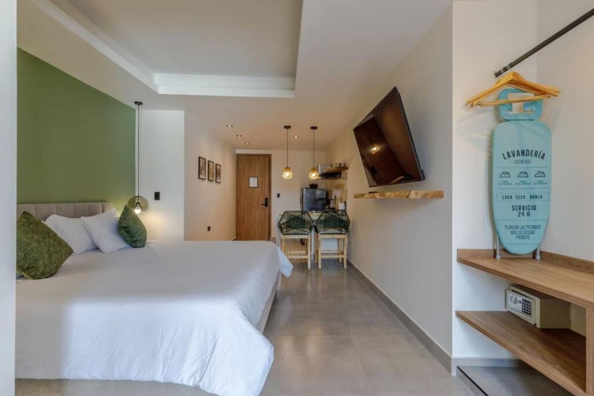 Un dormitorio con una cama, un televisor montado en la pared, una mesita con sillas y un estante con un objeto colgando.