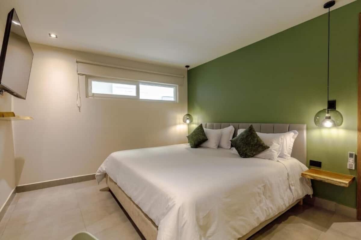 Un dormitorio ordenado con cama, mesitas de noche, televisor y ventana.