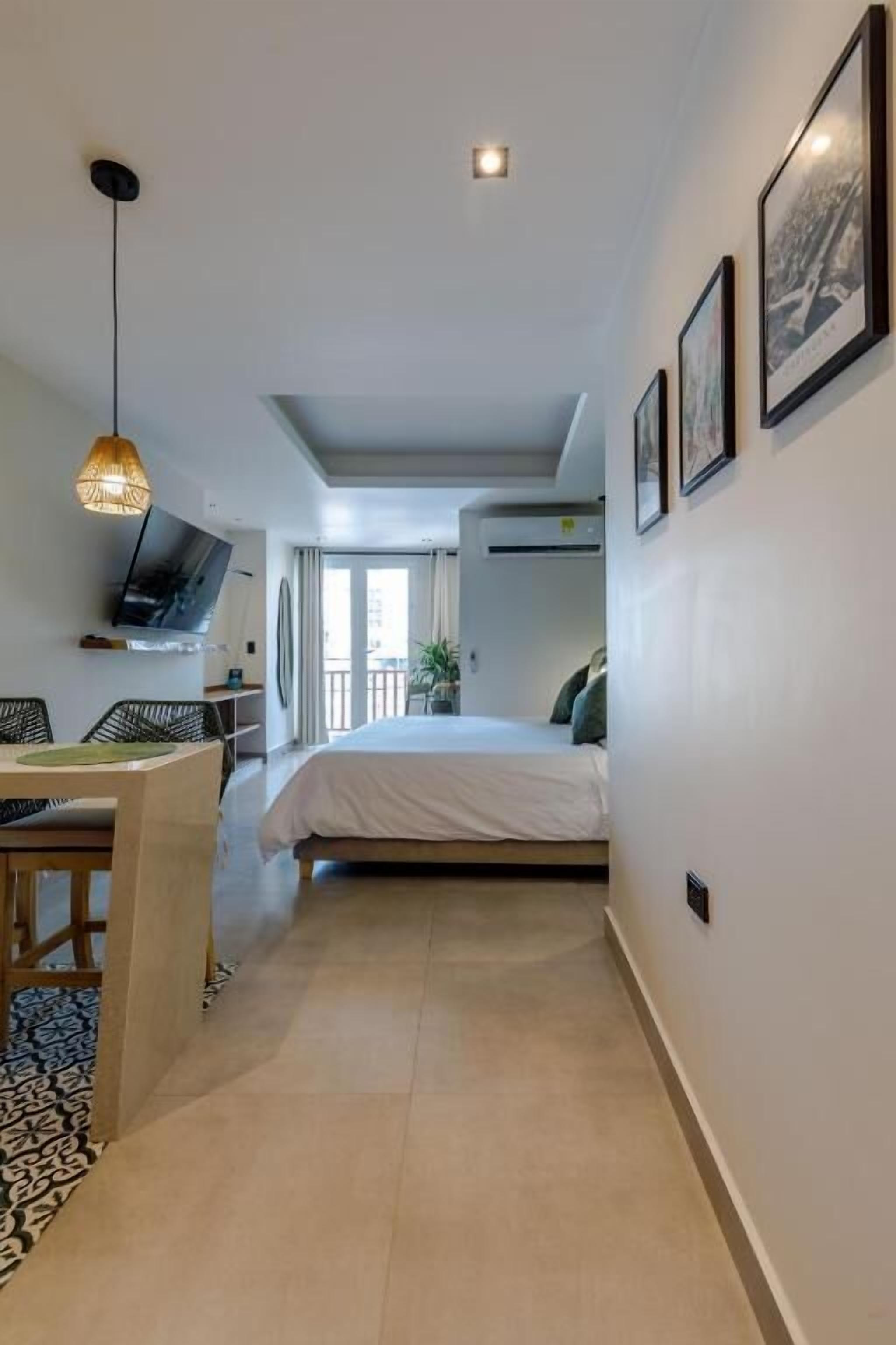 A modern hotel room with a bed, a TV, a dining area, and a balcony.