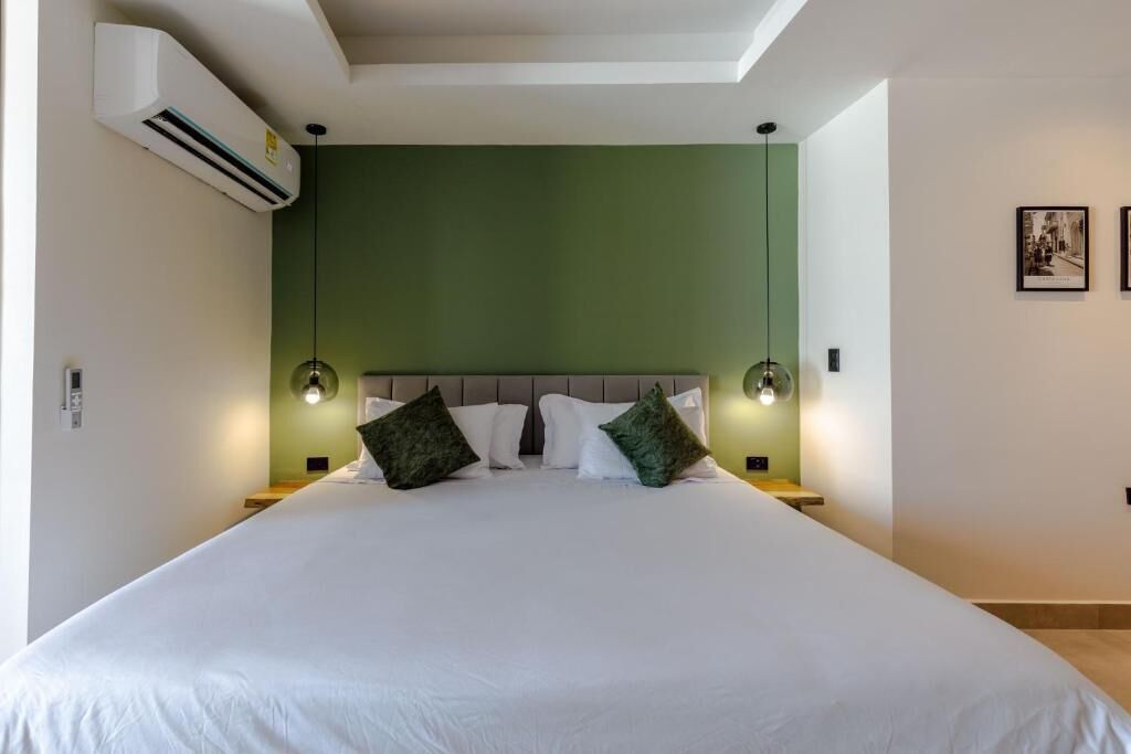 A neatly made bed with white linens, a green accent wall, and two bedside lamps.