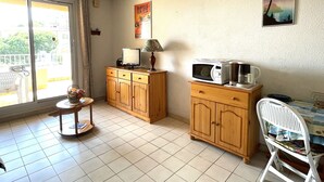 Una cocina con armarios de madera, un microondas, una mesita con lámpara y una silla.
