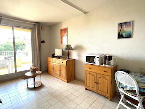 A kitchen with wooden cabinets, a microwave, a small table with a lamp, and a chair. - Cozy studio, sea view - 2 guests (Banyuls-sur-Mer)