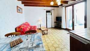 Un soggiorno accogliente con soffitto in legno, un divano rosso, un tavolino con quotidiani e una televisione nell'angolo.