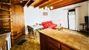 Una stanza accogliente con soffitto in legno, un tavolo da pranzo con sedie, un divano rosso e un televisore.