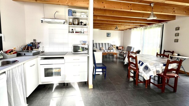 Een moderne keuken met witte kastjes, een ingebouwde magnetron en een eethoek met een houten tafel en stoelen.
