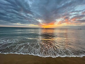 Une plage où les vagues viennent doucement lécher le rivage, sous un ciel flamboyant au coucher du soleil.