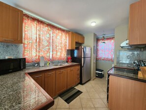 Una cocina con encimeras de granito, gabinetes de madera, un refrigerador de acero inoxidable, un microondas y una cafetera.