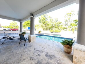 Un espacio al aire libre techado con piscina, sillones de descanso y una planta en maceta.