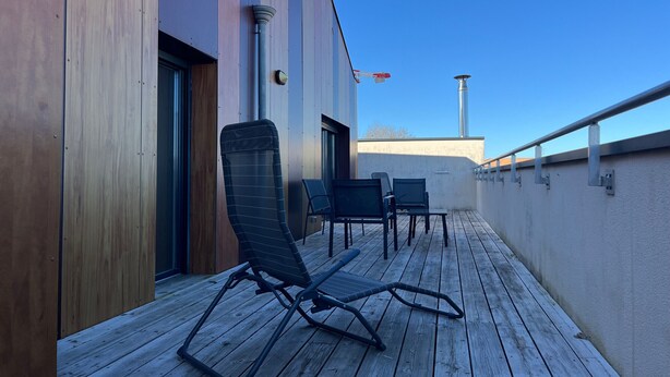 Eine Holzterrasse mit Sitzgelegenheiten im Freien und ein Gebäude im modernen Stil.