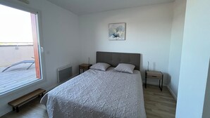 Ein Schlafzimmer mit einem Bett, zwei Nachttischen, einem Heizkörper, einer Bank und einem Fenster.