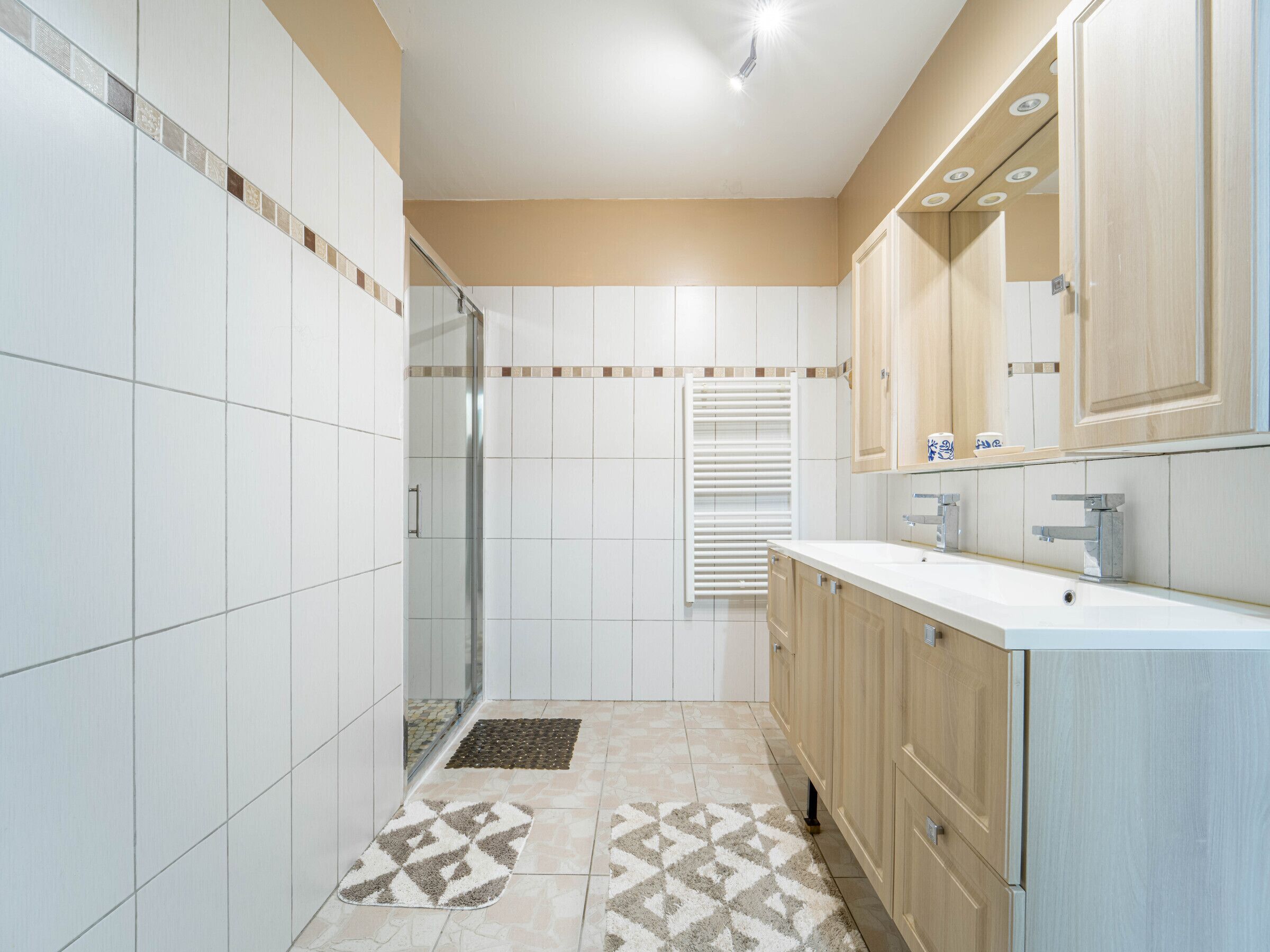 Une salle de bain moderne avec des carreaux blancs, une douche, un lavabo avec un miroir et des meubles en bois.