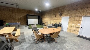 Huone, jossa on pingispöytä, projektorikangas, lava ja ovi.