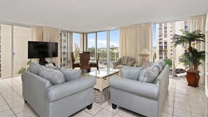 Ein geräumiges Wohnzimmer mit zwei grauen Sofas, einem Couchtisch, einem Fernseher und einem Balkon mit Stadtblick.