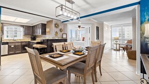 Une cuisine spacieuse avec des meubles de couleur sombre en bois, un grand îlot central et un coin repas comprenant une table et des chaises en bois.