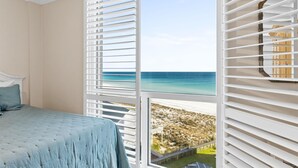 Une chambre avec un lit, une vue sur la plage et un balcon avec des stores blancs.