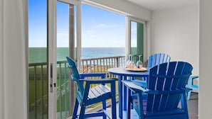 A balcony with a view of the ocean, blue chairs, and a small table with decorative items.