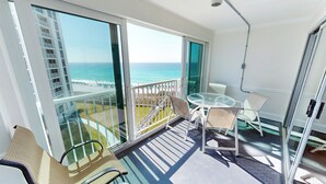 Un balcon avec une porte vitrée, une table avec des chaises et une vue sur la plage et l’océan.