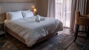 A neatly made bed with white linens, a bedside lamp, and a chair to the right. - Spacious 4-bedroom house on a private game farm in Limpopo, South Africa (LP)