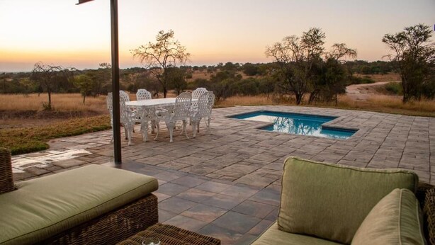 An outdoor patio with a pool, wicker furniture, and a view of the savanna at sunset. - Spacious 4-bedroom house on a private game farm in Limpopo, South Africa (LP)