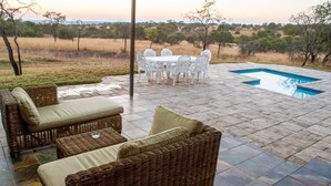 A patio with wicker furniture, a pool, and a view of the savannah. - Spacious 4-bedroom house on a private game farm in Limpopo, South Africa (LP)
