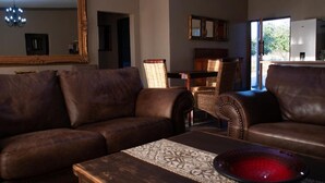 A living room with a brown leather sofa, a wooden coffee table with a patterned runner, and a red bowl. - Spacious 4-bedroom house on a private game farm in Limpopo, South Africa (LP)