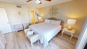 Une chambre à coucher avec un grand lit, deux tables de chevet, un fauteuil en osier et des œuvres d’art décoratives accrochées au mur.