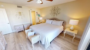 Ein Schlafzimmer mit einem großen Bett, zwei Nachttischen, einem Korbstuhl und dekorativer Wandkunst.
