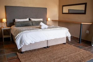 A neatly made bed with a grey headboard, two bedside lamps, and a woven rug on a tiled floor.