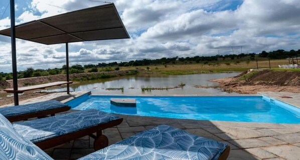 A swimming pool with lounge chairs and a canopy, surrounded by a natural landscape.
