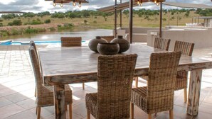 Comedor con una mesa redonda, sillas de mimbre y vistas a una piscina y al paisaje.