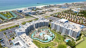 Vista aérea de um resort com vários edifícios, uma área de piscina central e uma praia ao fundo.