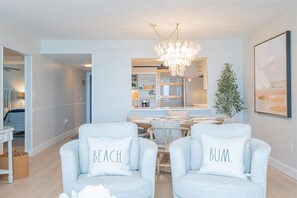 Ein modernes Wohnzimmer mit einer Kronleuchter, zwei Sesseln mit Kissen, einem Esstisch und einer Pflanze.