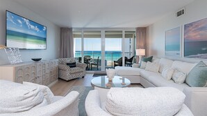 Ett modernt hotellrum med en balkong med utsikt över havet, en stor målning som föreställer havet och en mysig sittgrupp med ett soffbord.