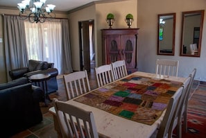 A dining area with a large table, white chairs, a dark sofa, and a cabinet with decorative items.