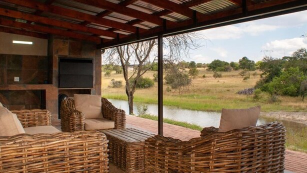 Een overdekt terras met rieten meubilair en uitzicht op een waterpartij en landschap.