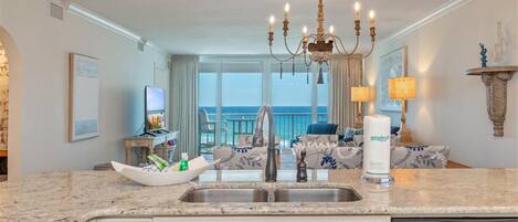 A modern kitchen with a granite countertop, a built-in dishwasher, and a view of the ocean through large windows.