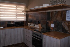 A kitchen with a microwave, toaster, kettle, and oven. There is a shelf with cups and glasses above the counter.