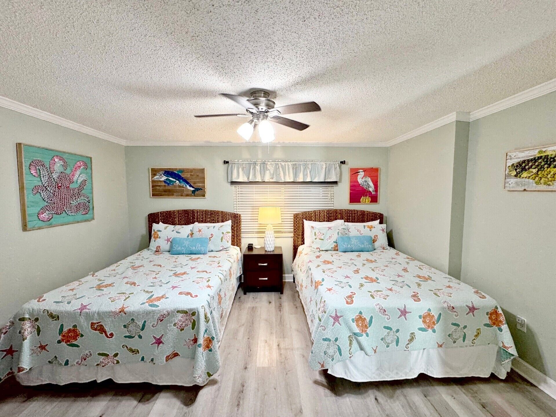 A bedroom with two beds, a ceiling fan, and artwork on the walls.