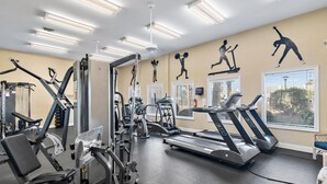 Et fitnesscenter med forskellig træningsudstyr, herunder løbebånd, styrkemaskiner og en væg med træningssilhuetter.