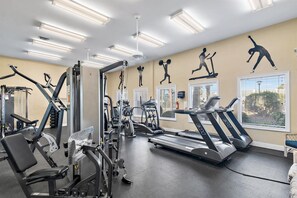 A gym with various exercise equipment, including treadmills, weight machines, and a wall with fitness silhouettes. - Splendid Views from Shoreline Towers 3112 (Destin)